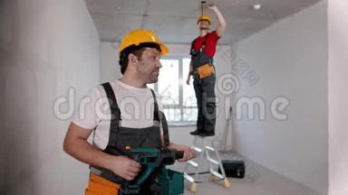 <strong>选秀</strong>室的公寓维修-一名男子工人站在摄像机前，把钻头递给另一个人